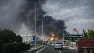 Thick black smoke rising in a Gulf city as vehicles drive along a highway following a reported strike targeting US-linked assets