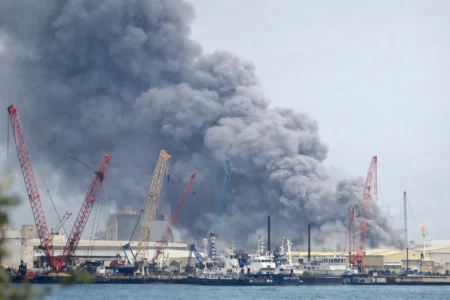 Gulf States Weigh Response After Iran Strikes Thick smoke rising above a port area in Manama, Bahrain, with cranes and docked vessels visible in the foreground