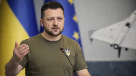 Ukrainian President Volodymyr Zelensky speaking at a podium during a press briefing with Ukraine flag in background