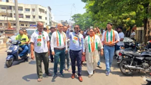 Congress workers wearing tricolor scarves lead a street march in a busy urban area with supporters and vehicles around
